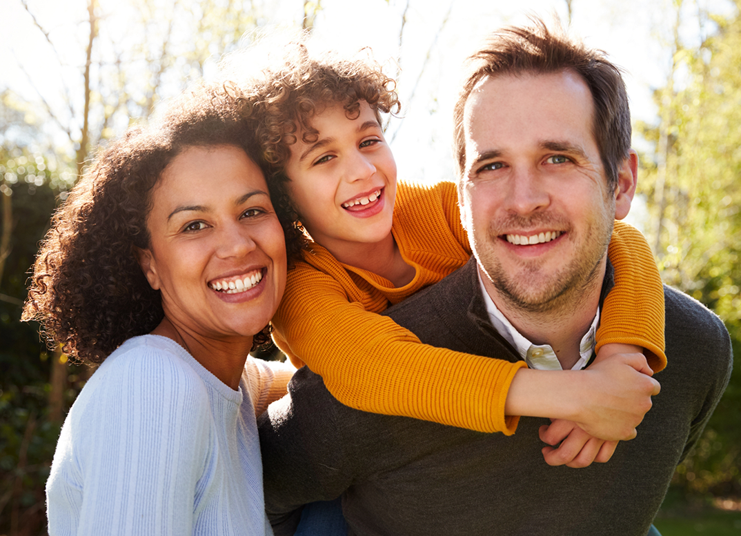 Family of three smiling in the sun