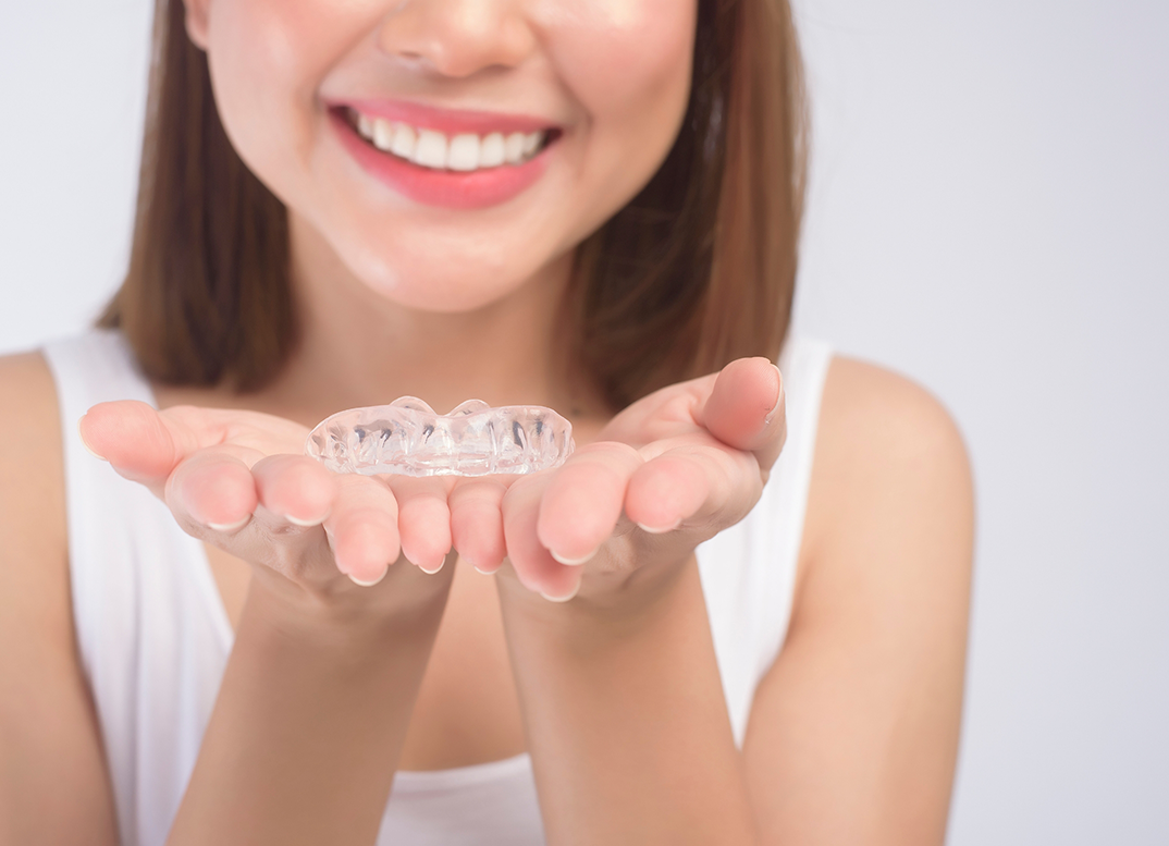 Smiling woman holding two Invisalign clear aligners in her open palms