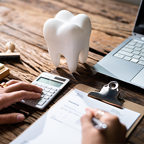 Person filling out paperwork at a desk with a model of a tooth