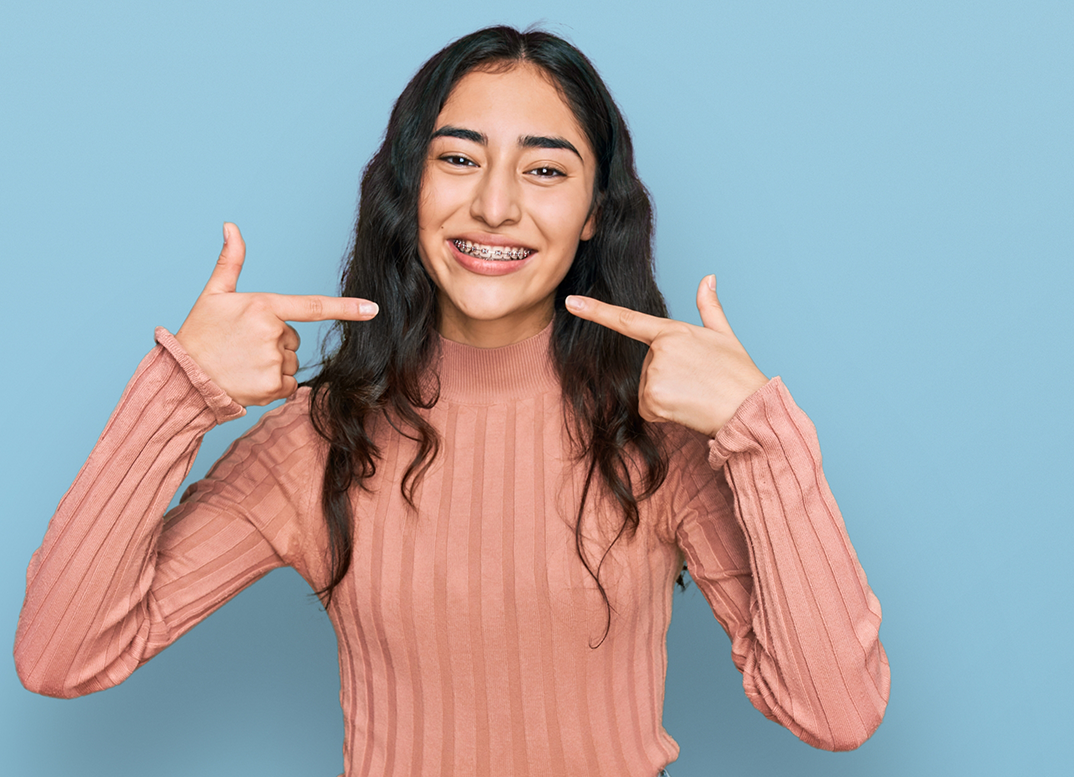 Teenage girl with braces pointing to her smile