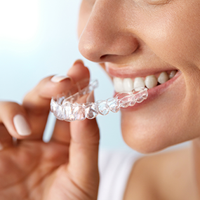 Person holding a clear aligner near their teeth