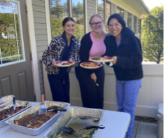 Three team members holding plates at an outdoor event with tables of food